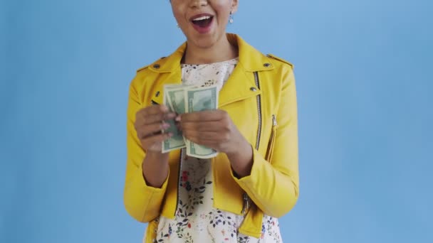 Attractive Afro american woman is counting money against a blue background Yellow jacket - Materiał filmowy, wideo