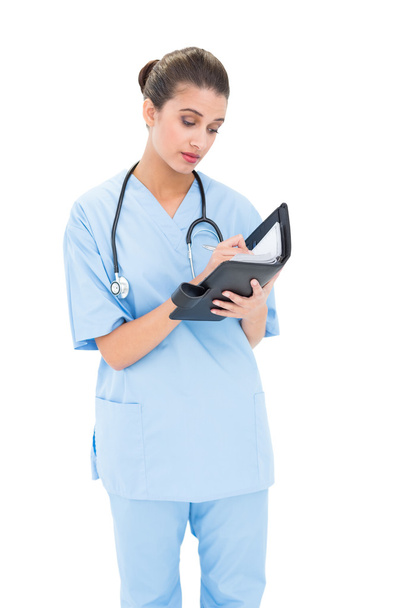 Concentrated nurse in blue scrubs filling an agenda - Фото, зображення