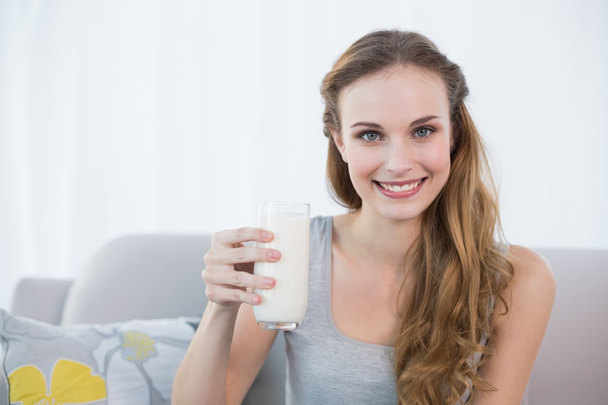 šťastná mladá žena sedící na gauči drží sklenici mléka - Fotografie, Obrázek