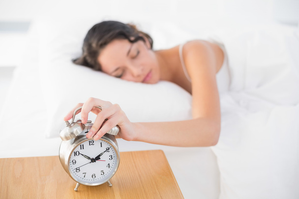 Calm casual brunette in white pajamas turning off her alarm clock - Foto, immagini