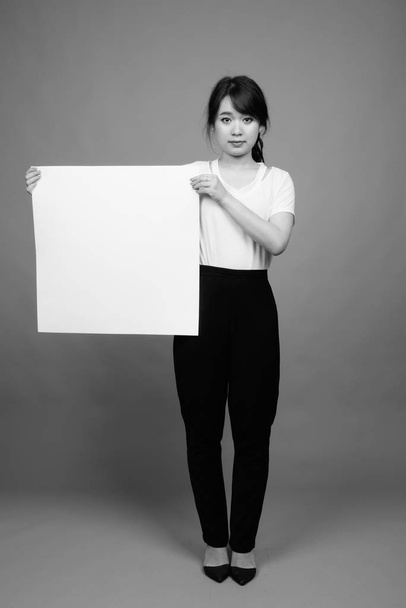 Studio shot of young beautiful Asian businesswoman against gray background in black and white - Φωτογραφία, εικόνα