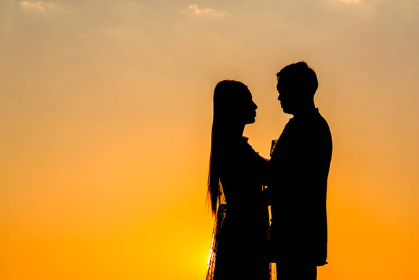 Sylwetka kochanków trzymających się za ręce - przytulających się o zachodzie słońca, - Zdjęcie, obraz
