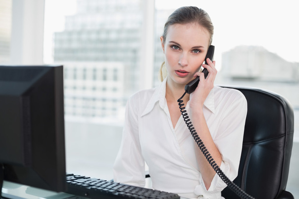 Stern businesswoman sitting at desk on the phone - Foto, Imagen