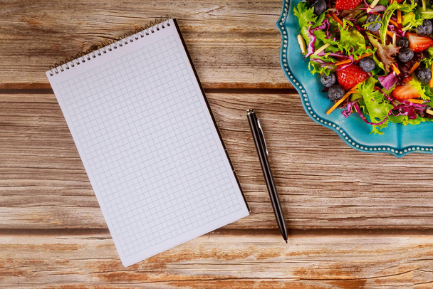 Notepad and pen with salad on wooden background. - Photo, Image