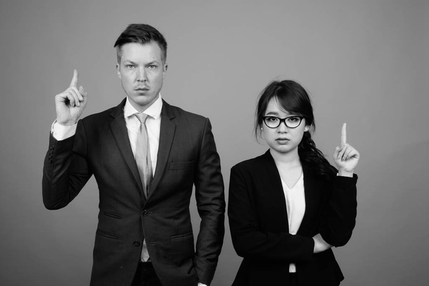 Студийные кадры молодых многонациональных деловых пар, работающих вместе на сером фоне в черно-белом - Фото, изображение