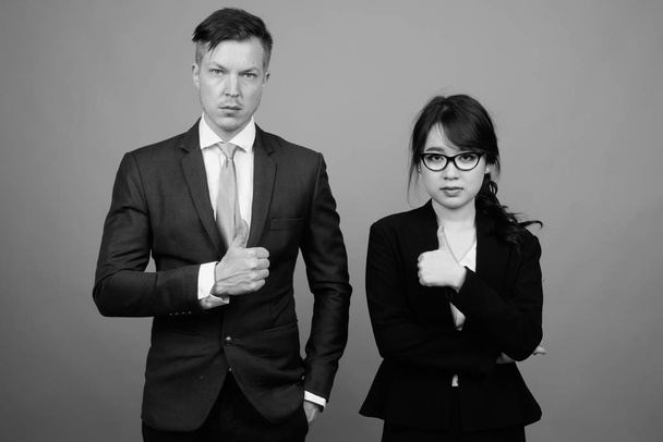 Studio shot van jonge multi-etnische business paar samen te werken tegen grijze achtergrond in zwart-wit - Foto, afbeelding