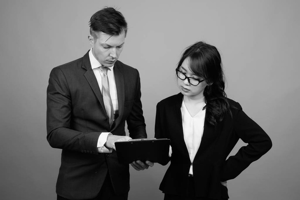 Estudio de una joven pareja de negocios multiétnicos trabajando juntos sobre un fondo gris en blanco y negro - Foto, Imagen