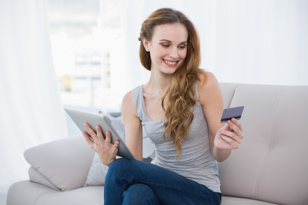 Pretty young woman sitting on couch using tablet - Foto, Bild