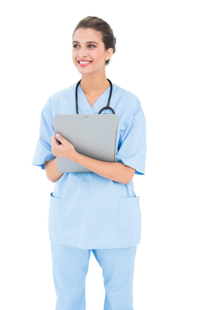 Thoughtful nurse in blue scrubs holding a clipboard - Photo, image