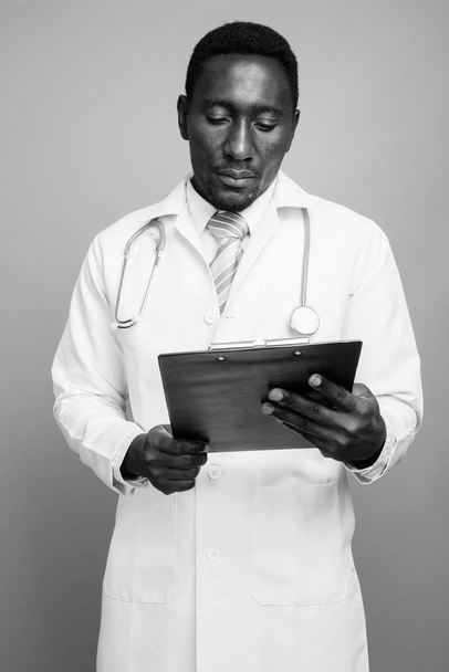 młody przystojny Afryki mężczyzna lekarz na szarym tle - Zdjęcie, obraz