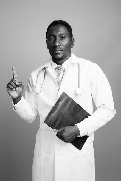 Young handsome African man doctor against gray background - Foto, Imagen