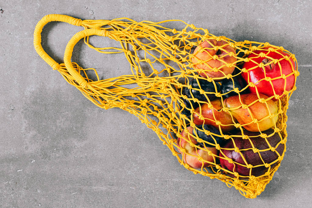Still life of yellow biodegradable shopping bag with raw fruit on gray background, top view, flat lay - 写真・画像