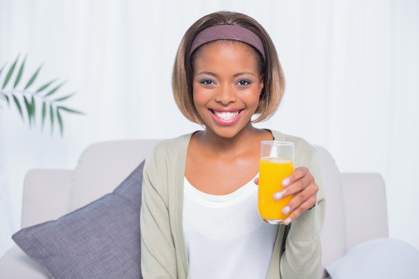 オレンジ ジュースのガラスを保持しているソファに座っている女性の笑みを浮かべてください。 - 写真・画像