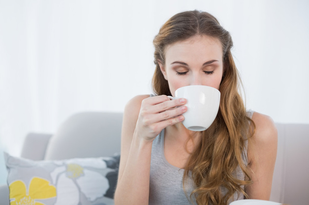 Cheerful young woman sitting on sofa drinking from cup - Foto, imagen