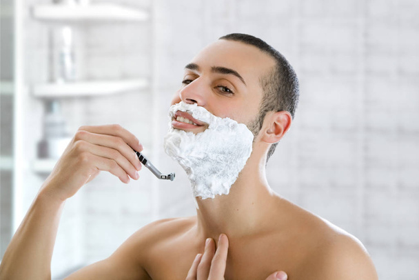handsome man shaving his beard in the bathroom - Foto, afbeelding