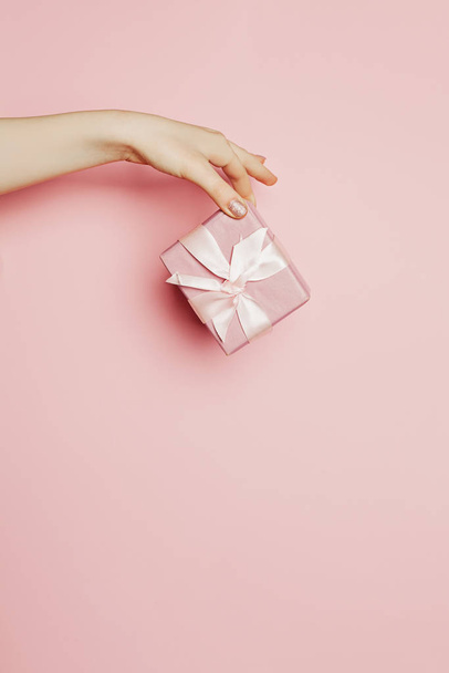 Mano femenina dando caja de regalo rosa con cinta sedosa y lazo
  - Foto, imagen