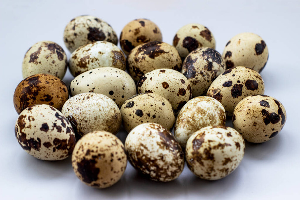 Group of quail eggs on a white background. A lot of spotted eggs on a light background, close-up. - Foto, afbeelding