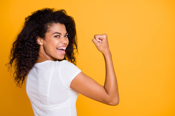Photo of brunette haired cheerful cute nice curly wavy trendy youngster showing the power in her muscular arm shouting satisfied about her achievement isolated vivid color background in white t-shirt - 写真・画像
