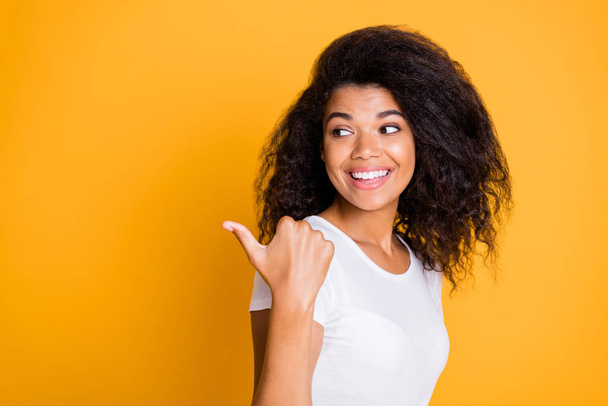 Photo of cheerful positive nice pretty girlfriend pointing at empty space with thumb smiling toothily in white t-shirt isolated vivid color background - Fotoğraf, Görsel