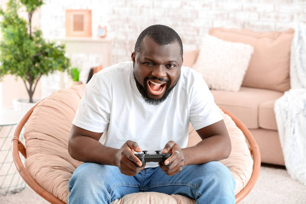 Duygusal Afro-Amerikalı adam evinde koltukta otururken video oyunu oynuyor. - Fotoğraf, Görsel