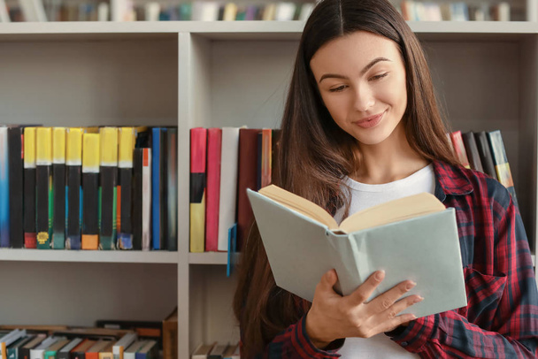 Vrouwelijke student lezen boek tijdens de voorbereiding van het examen in de bibliotheek - Foto, afbeelding