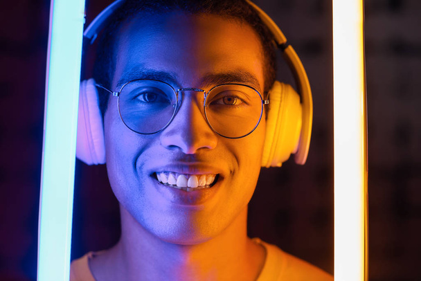 Toned portrait of African-American man with headphones and neon lamps on dark background - Foto, imagen