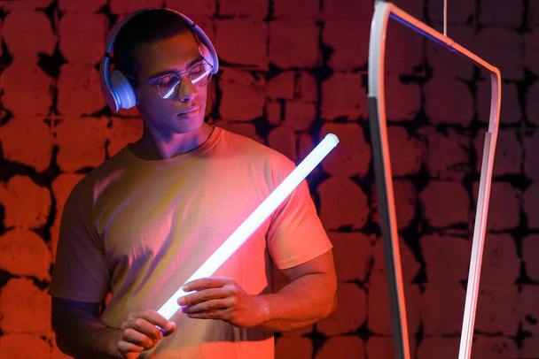 Toned portrait of African-American man with headphones and neon lamp on dark color background - Foto, afbeelding