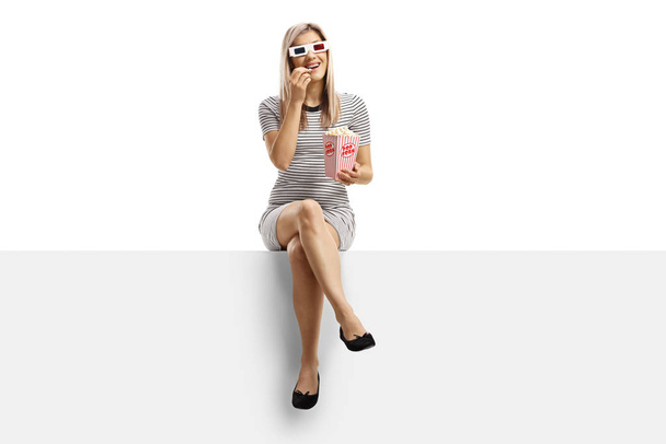 Donna seduta su un pannello bianco con una scatola di popcorn e indossa
 - Foto, immagini