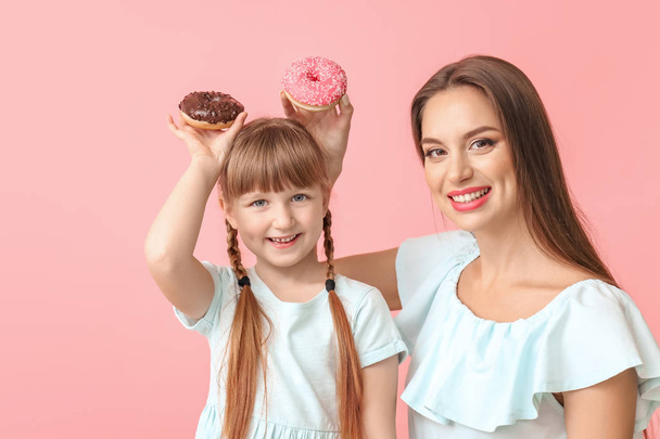 Beautiful young woman and little girl with donuts on color background - Photo, Image