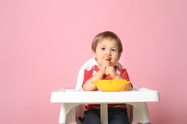Cute little boy eating tasty baby food against color background - Photo, Image