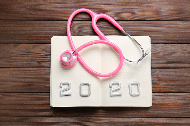 Stethoscope, notebook and figure 2020 on wooden background - Zdjęcie, obraz