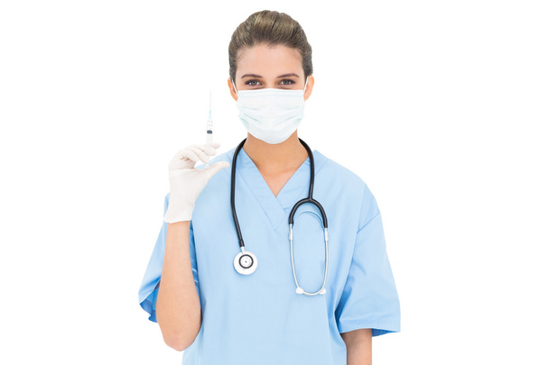 Cute nurse in blue scrubs wearing a protective mask and holding a syringe - Zdjęcie, obraz