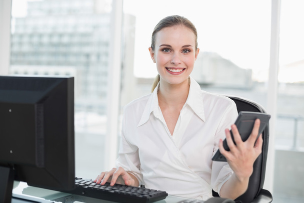 Happy businesswoman holding calculator sitting at desk - Фото, зображення