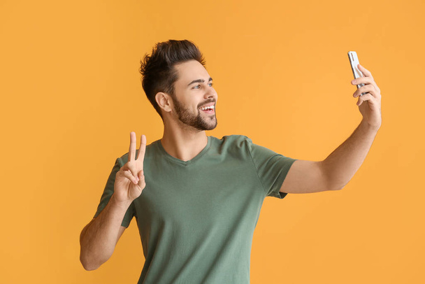 Happy young man taking selfie with mobile phone on color background - Фото, зображення