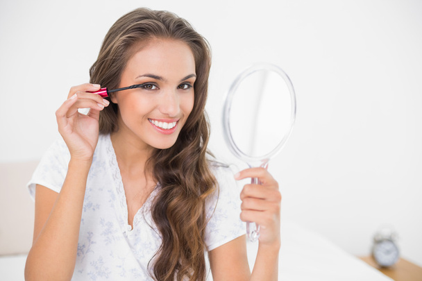 Brunette applying mascara and holding mirror - Foto, imagen