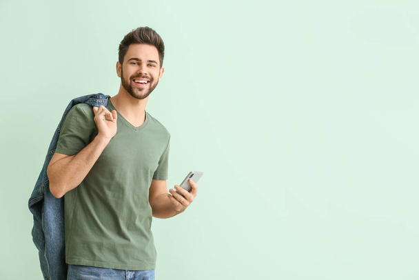 Glücklicher junger Mann mit Handy auf farbigem Hintergrund - Foto, Bild
