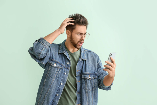 Geschokte jongeman met mobiele telefoon op kleur achtergrond - Foto, afbeelding