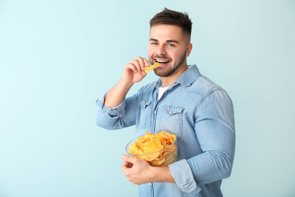 Bello giovane uomo con gustose patatine su sfondo di colore
 - Foto, immagini