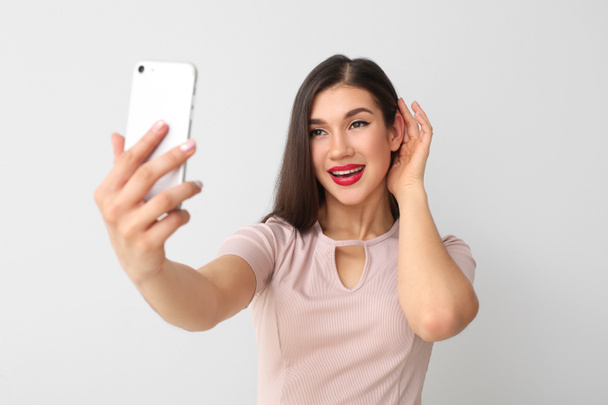 Beautiful young woman taking selfie on light background - Valokuva, kuva