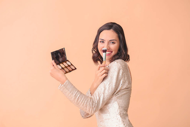 Beautiful young woman applying makeup on color background - 写真・画像