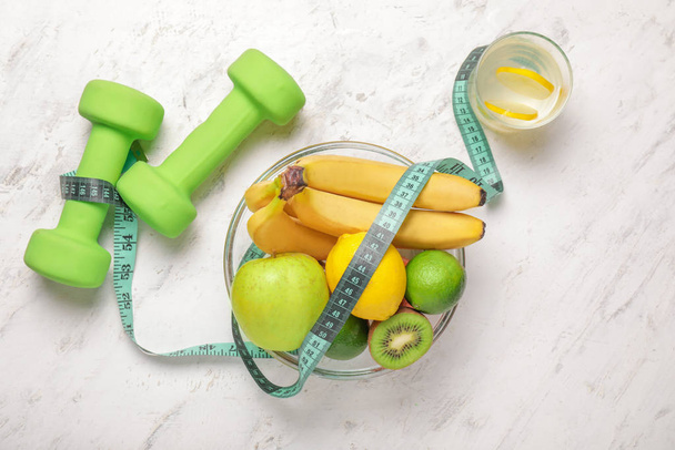 Different healthy food, dumbbells and measuring tape on light background. Diet concept - Zdjęcie, obraz