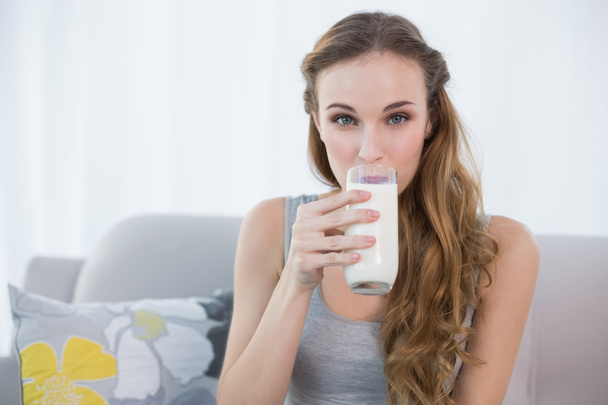 Happy young woman sitting on sofa drinking milk - Foto, imagen