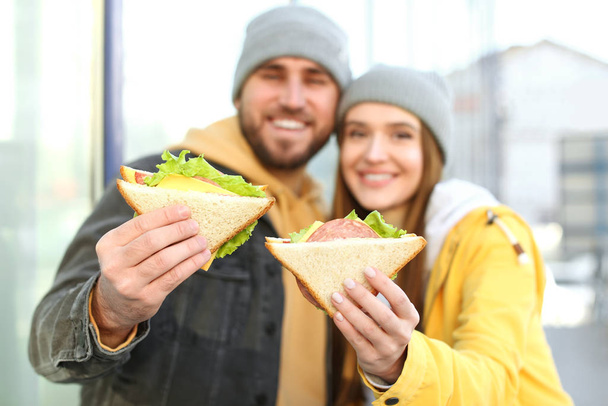 Happy young couple with sandwiches on city street - 写真・画像