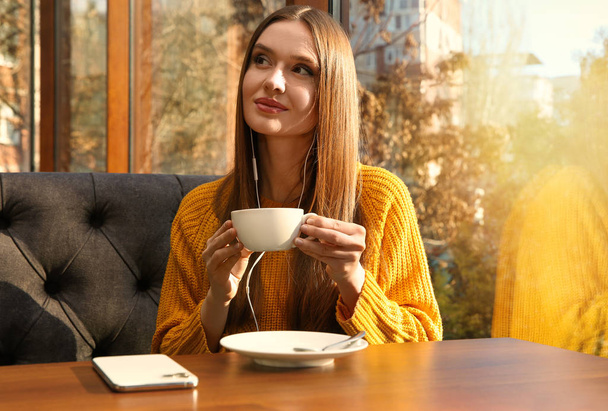 Žena poslouchající audioknihu u stolu v kavárně - Fotografie, Obrázek