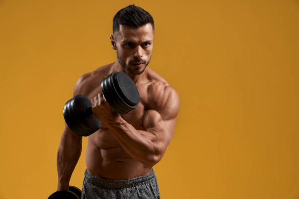Handsome bodybuilder pumping up arm muscles - Foto, Imagen