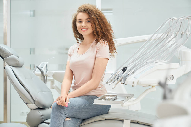 Smiling girl with curly hair sitting in dental chair - Foto, imagen