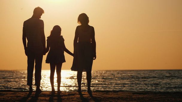 Młoda para z dzieckiem stoi na plaży, oglądając piękny zachód słońca - Zdjęcie, obraz