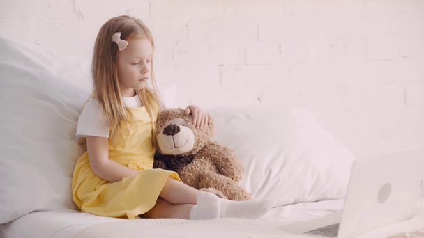 Kid kijken cartoons op laptop door teddy beer op bed  - Video