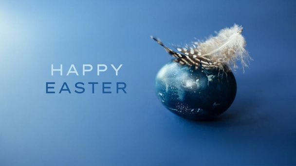 Oeuf de Pâques wirh plume sur fond bleu avec espace vide. Carte de Pâques
 - Photo, image