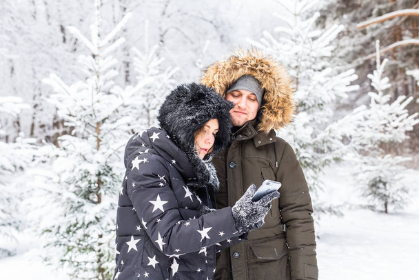 Technologies and relationship concept - Happy smiling couple taking a selfie in a winter forest outside - Photo, Image